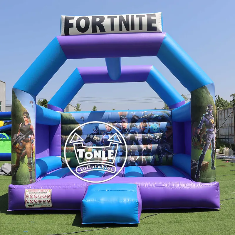 Blue and purple Fortnite themed inflatable bouncy castle with character graphics on side pillars and back wall, set on green artificial turf.
