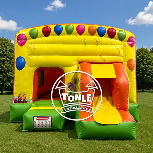 Yellow Multifun Party Bouncy Castle with balloon graphics and orange slide, measuring 5.3m x 3.6m, set up in a warehouse.