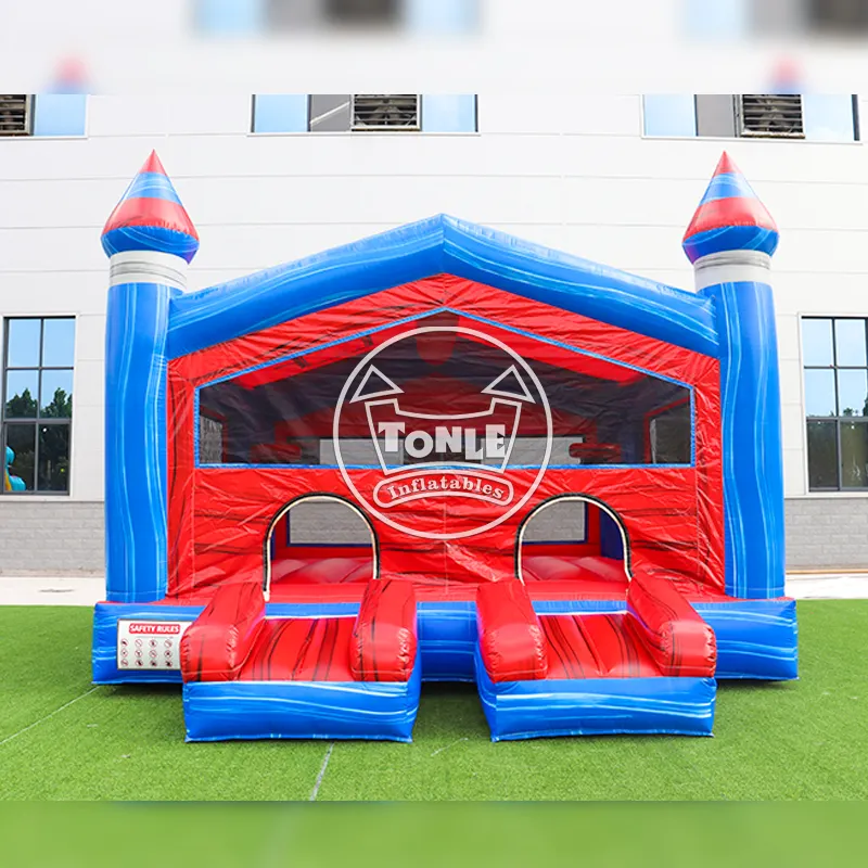 Front view of red and blue 6x5.4m inflatable bounce house with dual entry ramps and castle turrets on grass