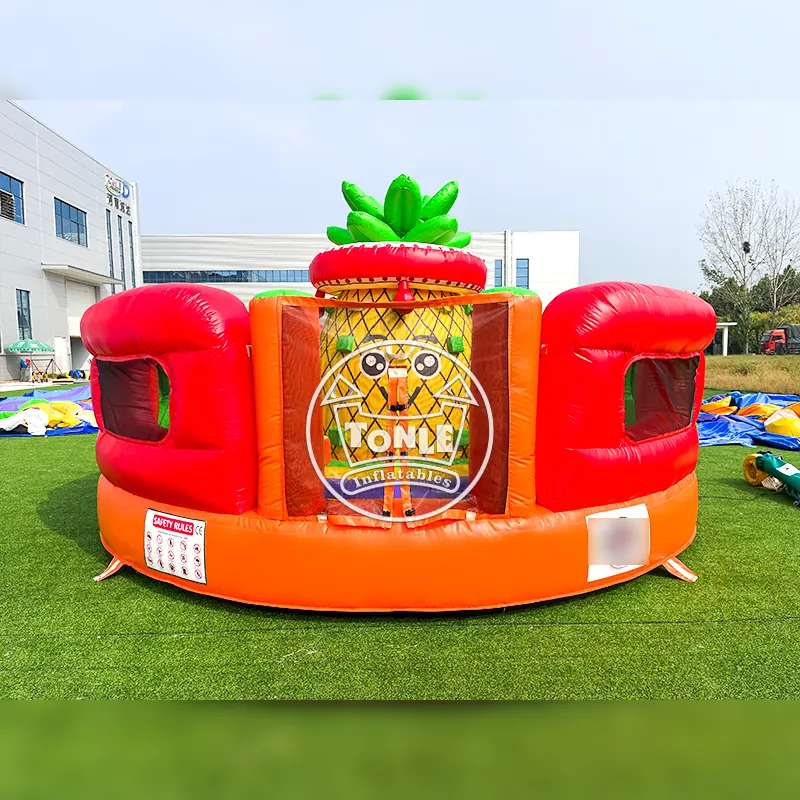 Front view of orange and red fruit-themed inflatable climbing wall with central pineapple column on grass