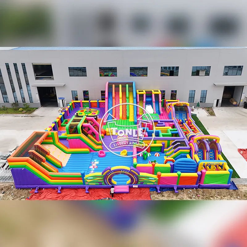 Aerial view of a massive 32x30m rainbow-colored inflatable theme park featuring multiple slides, obstacle courses, and a central play area constructed from 0.9mm PVC tarpaulin.