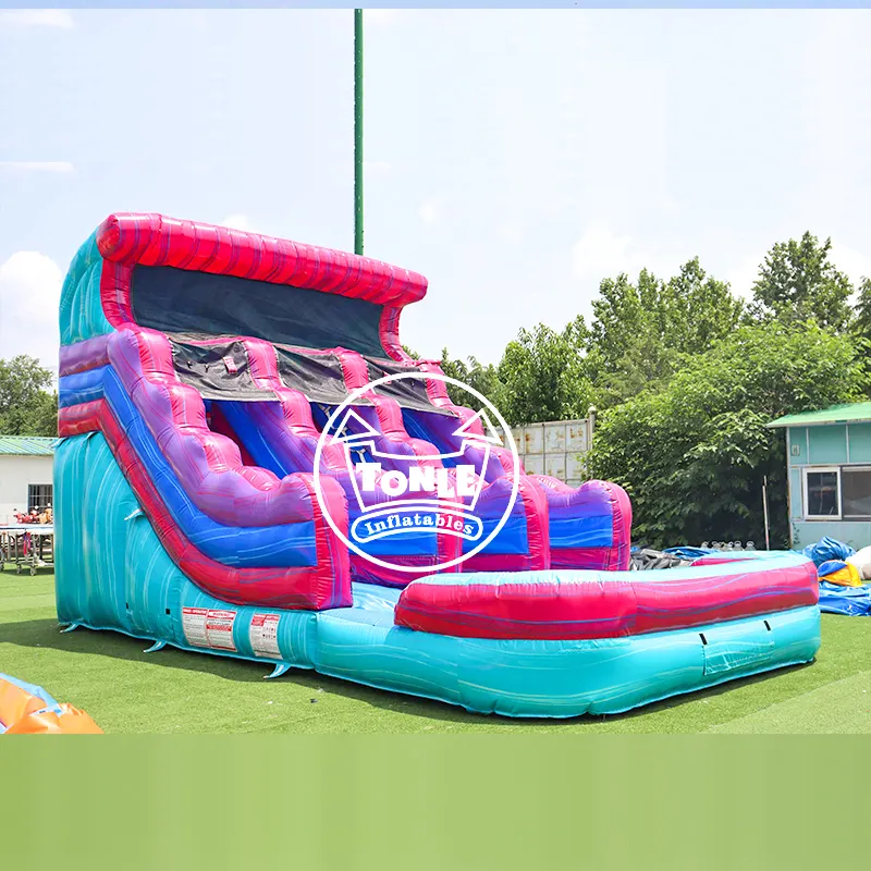 Commercial inflatable water slide with cyan and magenta wave design featuring dual lanes and splash pool