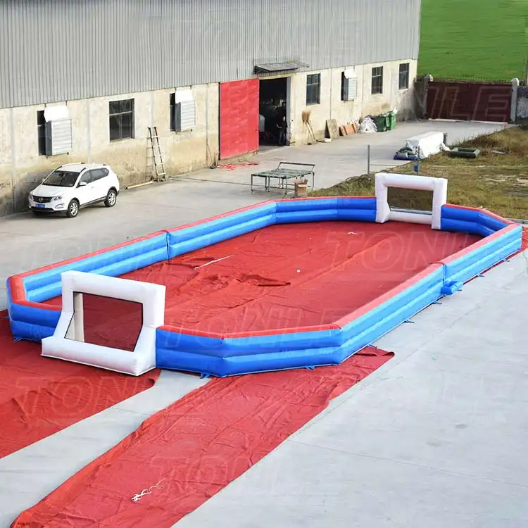 Red and blue 66x33ft inflatable soccer field with white goals on concrete
