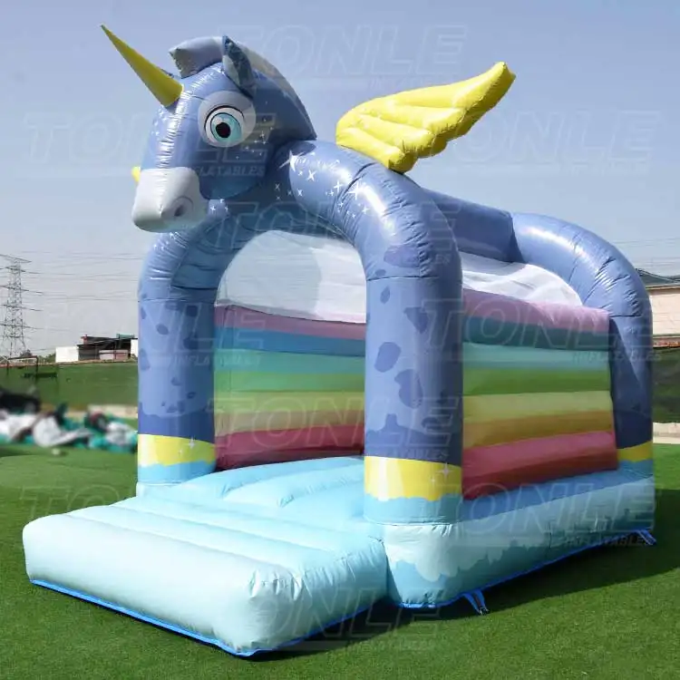 Blue unicorn themed bouncy castle with rainbow interior walls and yellow wings on grass