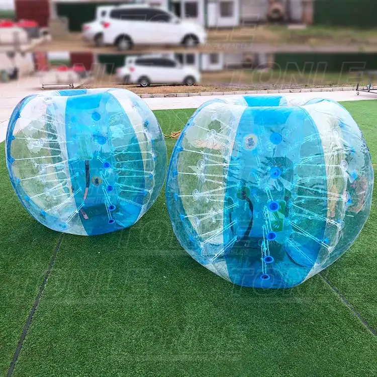 Two transparent blue 1.2m inflatable bubble balls on green artificial turf showing internal harness straps