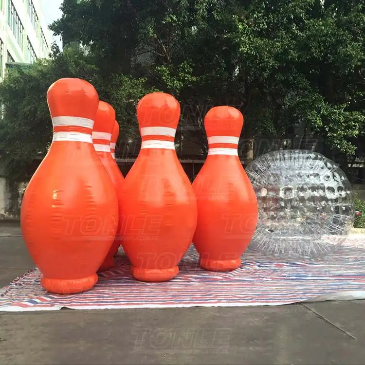 Giant orange inflatable bowling pins with white stripes and a clear zorb ball on a striped tarp