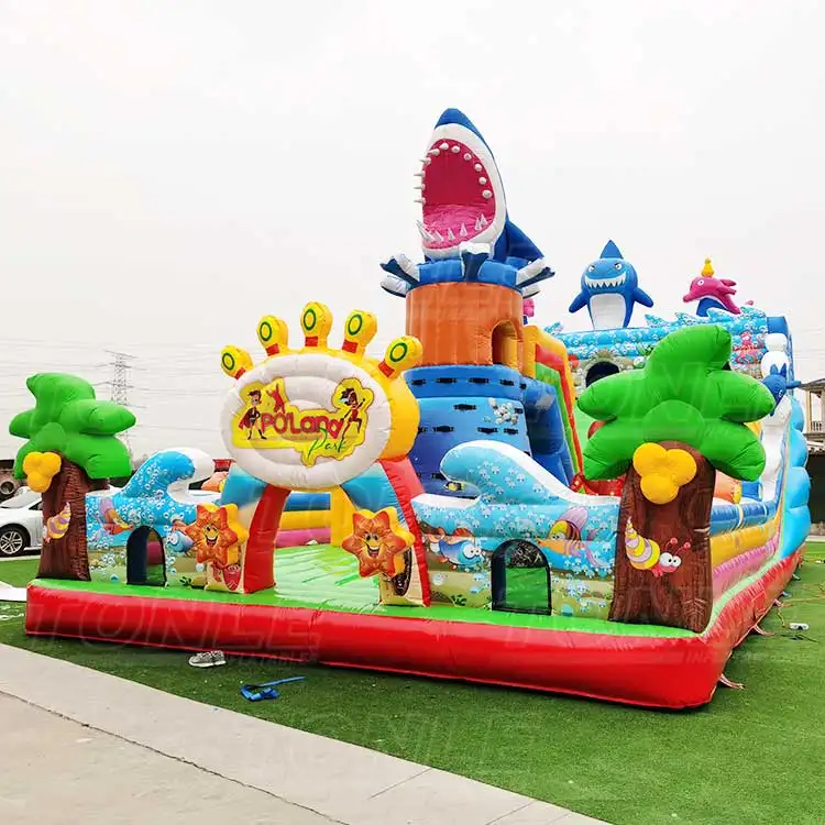 Ocean Shark Medium Playground inflatable featuring a large blue shark head tower, orange climbing section, and green palm trees on a red base