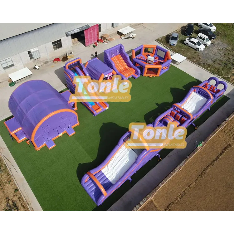Aerial view of a large purple and orange inflatable fun city with slides and tunnels on green turf