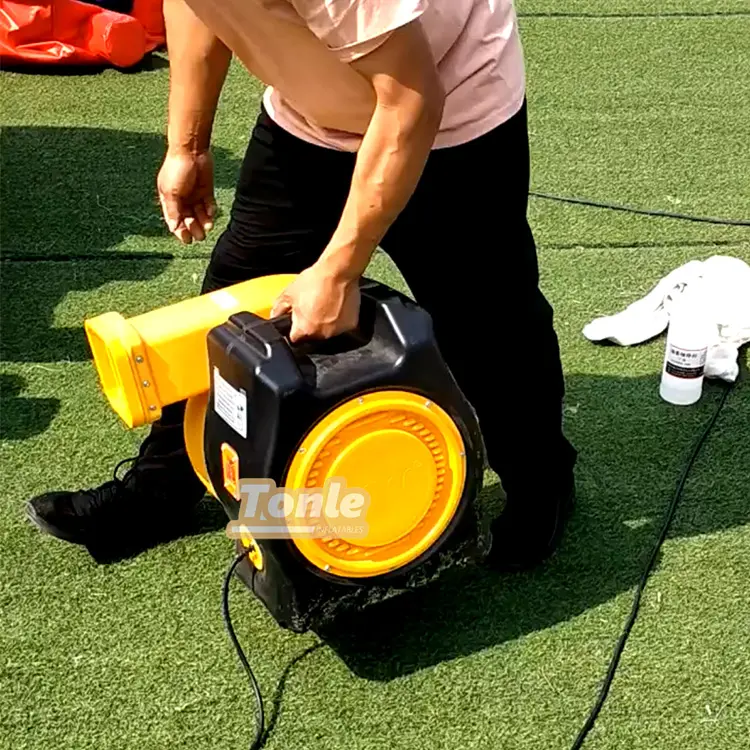 Person carrying black and yellow 3HP commercial air blower on artificial grass