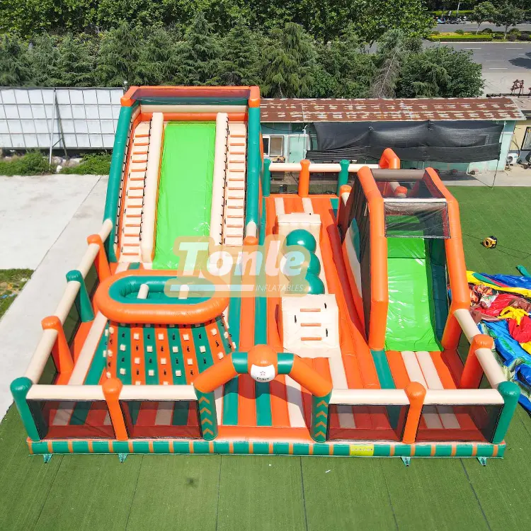 Aerial view of orange and green 15m inflatable obstacle course with dual slides and climbing wall