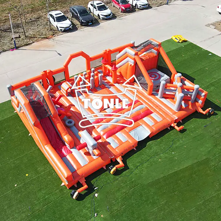 Aerial view of orange and grey 12.3m inflatable obstacle course with slide on green turf