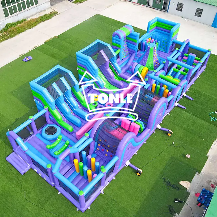 Aerial view of a 79ft purple and blue inflatable obstacle course with slides and climbing walls on green turf