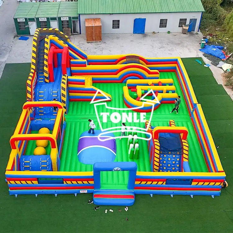 Aerial view of 18x16m inflatable fun park with red, yellow, and blue obstacles on green turf