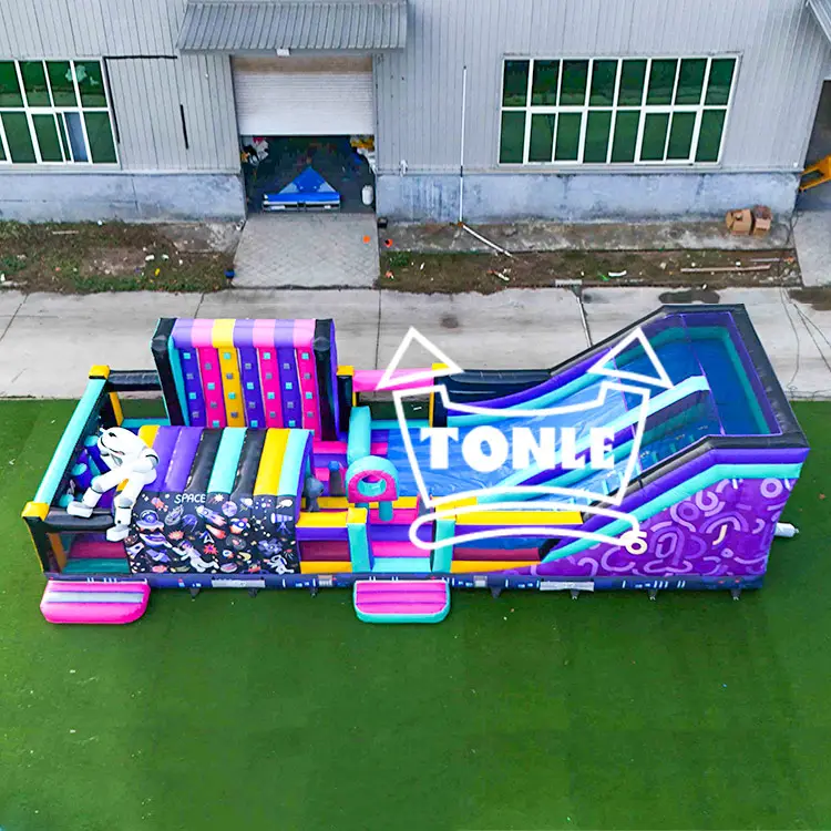 Aerial view of 14m purple and neon inflatable astronaut theme park with water slide and climbing wall on green turf