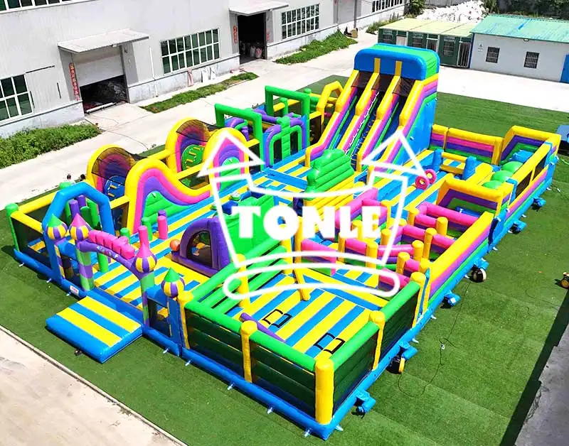 Aerial view of 23x16m inflatable fitness park with blue, green, and yellow obstacles on artificial turf