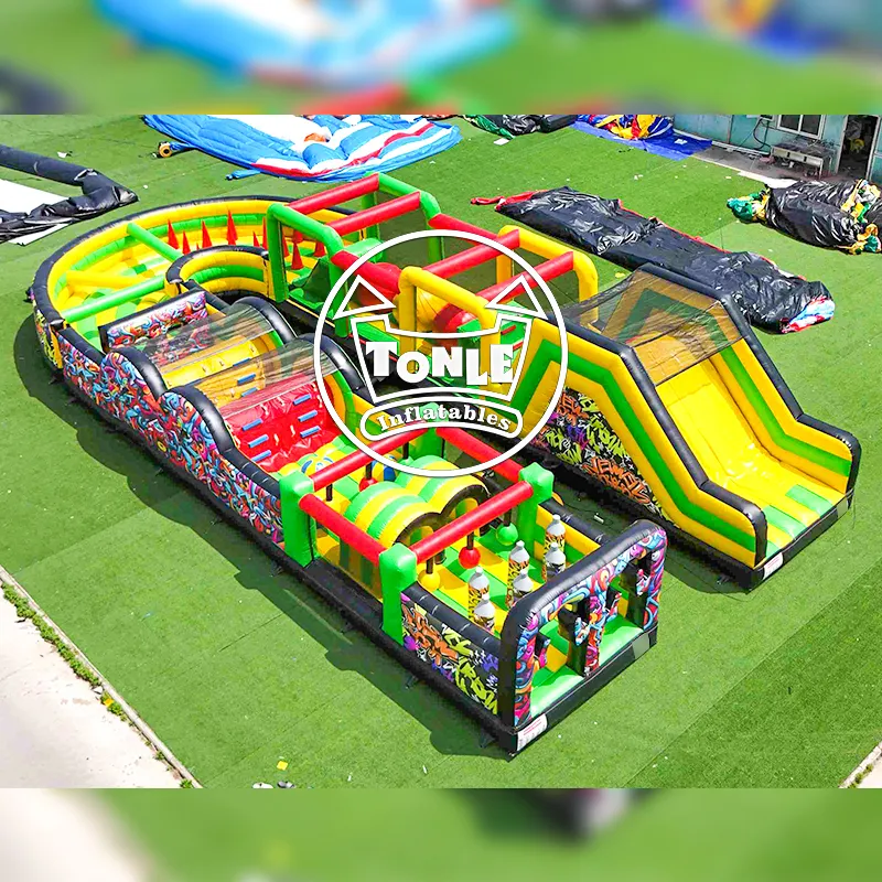 Aerial view of 18m U-shaped graffiti inflatable obstacle course with yellow slide and green barriers on artificial turf