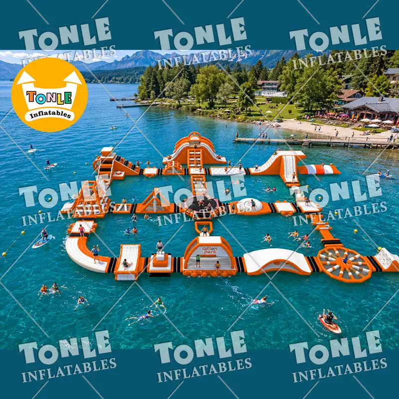 Aerial view of 38.5m orange and white floating water park on a lake with mountains in background